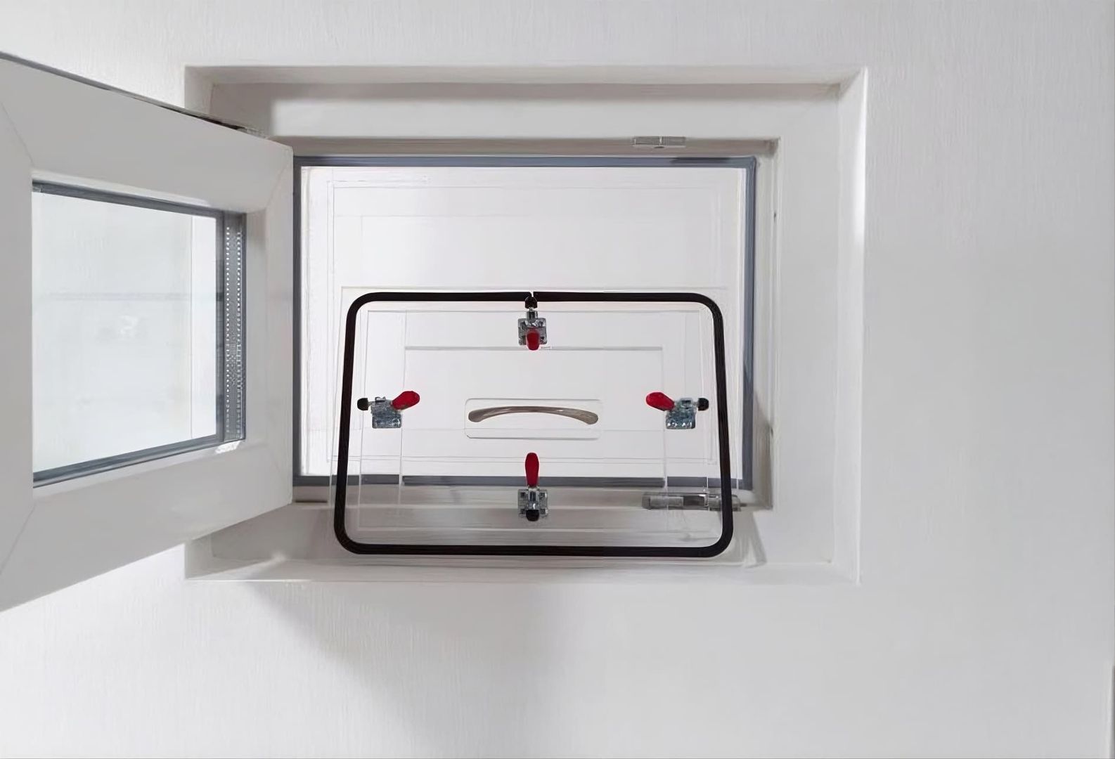 Geöffnetes Kellerfenster mit montiertem transparentem Insektenschutzgitter und roten Verschlusshebeln.